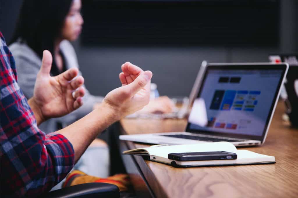 hands of a man explaining something, with laptop nearby. Symbolizes idea that a stock is only worth what someone will pay